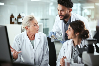 Three oncology researchers in lab coats discuss clinical trial data and emerging treatment strategies, reflecting collaboration in modern drug development.