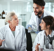 Three oncology researchers in lab coats discuss clinical trial data and emerging treatment strategies, reflecting collaboration in modern drug development.
